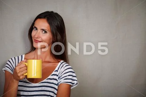 Waist up portrait of a brunette lady holding mug while looking at camera - co Stock Photos
