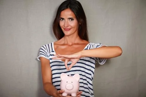 Waist up portrait of a happy woman in her 30s holding a piggy bank with savin Stock Photos