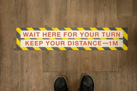 Wait your turn, keep your distance sign on a store floor. Stock Photos