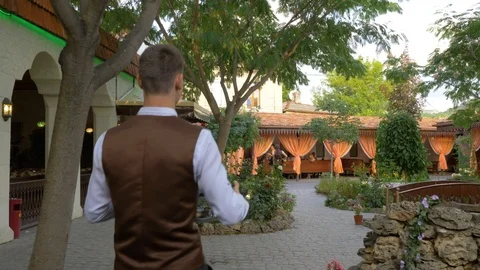 The waiter carries a dish to the table through a green oriental courtyard Stock Footage 124770660
