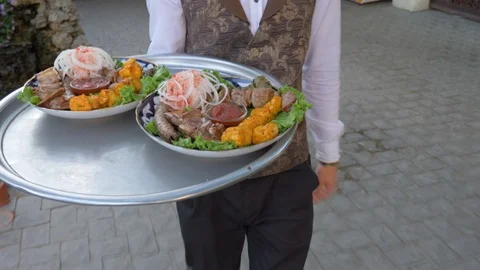 The waiter carries a dish to the table through a green oriental courtyard Stock Footage 124770665