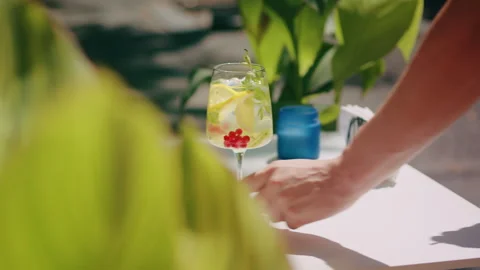 Waiter hand puts on a table beautiful refreshing fruit cocktail in a summer city Stock Footage 246477162