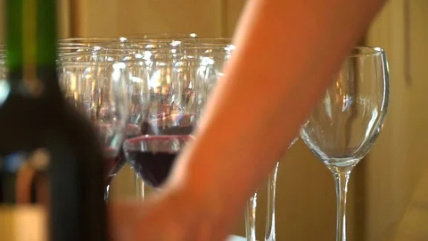 The waiter pours red wine in the rows of glasses.On the table is a bunch of red Stock Footage 92498795