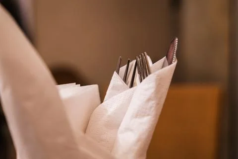 A waiter prepares elegant silverware for dining in a cozy restaurant setting Stock Photos