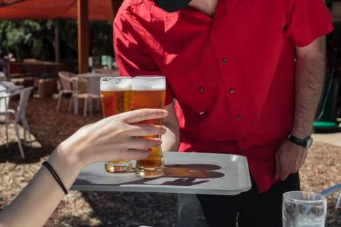 Waiter with protective mask on face serving beer to client at outdoor bar Stock Photos
