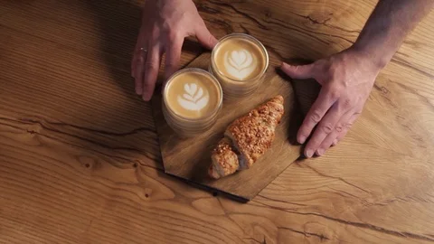 Waiter putting two cups of latte coffee with croissants on a table. Stock Footage 123363124