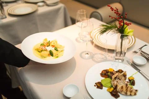 Waiter serves plate of ravioli on table Stock Photos
