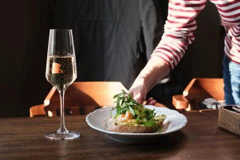 Waiter serving appetizer on restaurant table next to glass of sparkling wine Stock Photos
