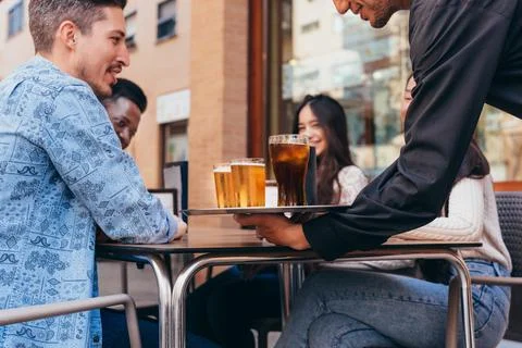 Waiter serving drinks at a table of friends of different ethnic backgrounds Stock Photos