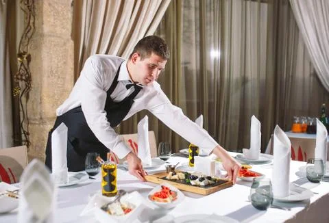 Waiter serving table in the restaurant preparing to receive guests. Stock Photos