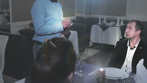 A waiter takes an order from a middle-aged couple in a restaurant and writes Stock Footage 97577538