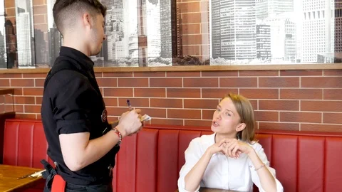 The waiter is taking the order from a young pretty girl in the restaurant Stock Footage 116435367