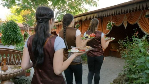The waiters carries a dish to the table through a green oriental courtyard Stock Footage 124770662