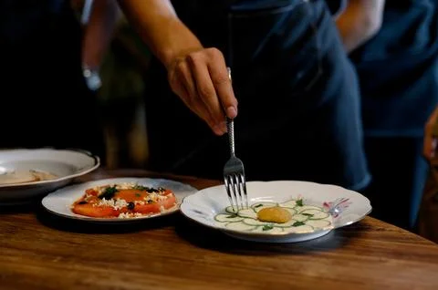 A waiter's hand with a fork decorates a plate with fresh vegetables. Stock Photos