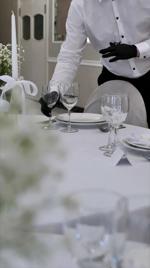 Waiter's hands laying out glasses on a festive table in a banquet hall Stock Footage 306750731