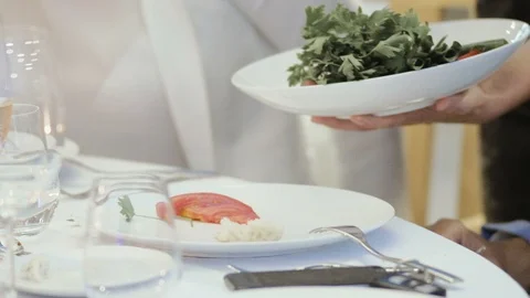 Waiter's hands put the salad in plates and meat snacks in the restaurant. Stock Footage 93377243