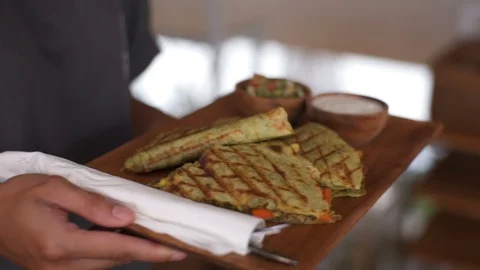 Waiter's hands put on the table Vegetable quesadils on a wooden round board Stock Footage 101636631