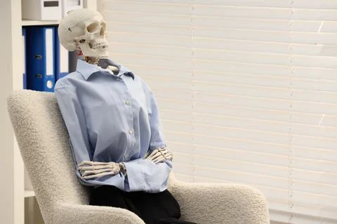 Waiting concept. Human skeleton sitting in armchair at office, space for text Stock Photos