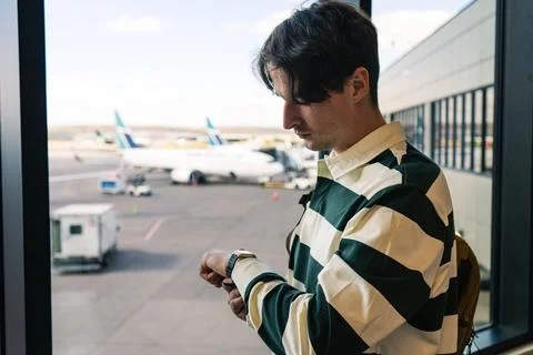Waiting for the flight, checking time with his watch at the airport gate. Stock Photos