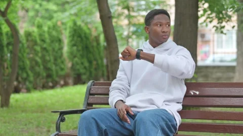 Waiting Young African Man Checking Time on Watch Outdoor on Bench Vidéo 311850047