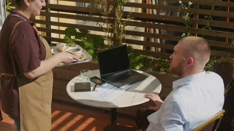 Waitress Bringing Order to Client Working on Laptop at Table in Outdoor Cafe Stock Footage 317376059