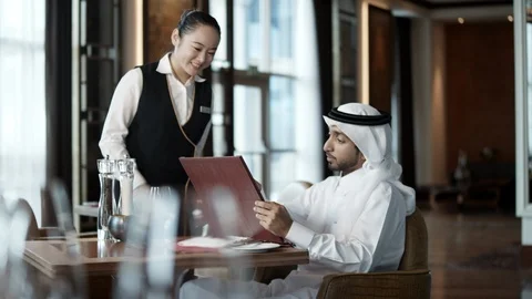 Waitress discussing over menu card with Arab man at restaurant. Stock Footage 119394172