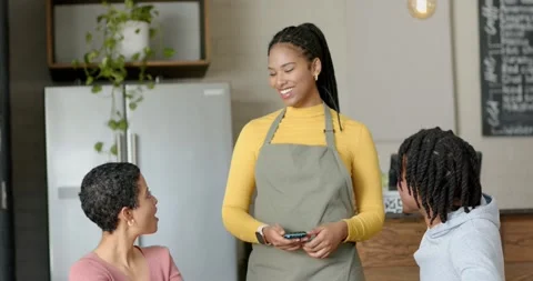 Waitress greeting couple at cafe, offering payment terminal, man tapping phone, 動画素材 345123669