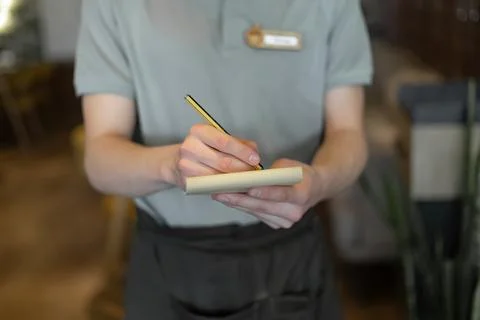Waitress hand noting down menu on notebook in cafe. Stock Photos