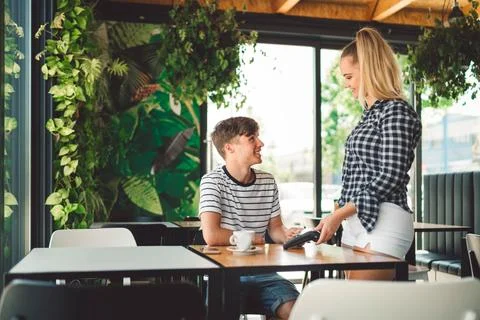 Waitress holding the card reader while young man costumer pays for his drink Stock Photos