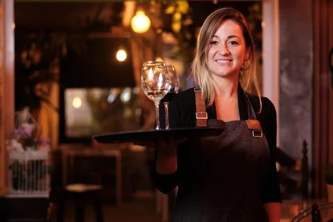 Waitress looking at the camera and smiling while holding a tray with wine Stock Photos