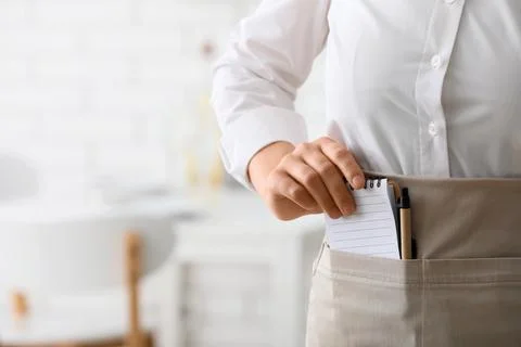 Waitress or barista pulling a notepad and pen from an apron pocket, restauran 스톡 사진