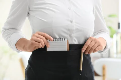 Waitress or server pulling a small notepad and pen from an apron pocket, read Stock-Fotos