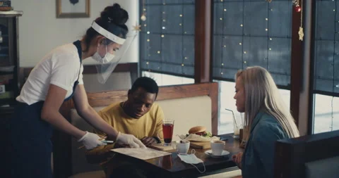 Waitress in self protection serving diverse couple in cafe Stock Footage 145709187