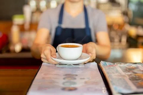 Waitress serving coffee while standing in coffee shop counter. Stock Photos