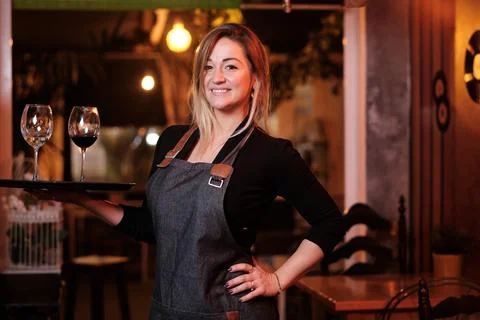 Waitress smiling while holding a tray with wine glasses in a restaurant. Stock Photos