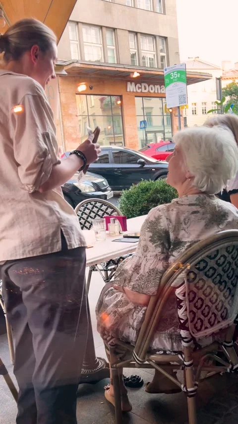 A waitress takes an order from two senior women sitting at an outdoor cafe. Stock Footage 346732637