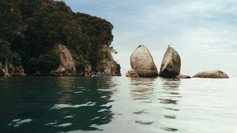 Waka rowing from behind large broken rock Stock Footage 107917476