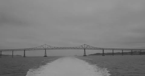 A wake forms behind a ferry moving away from a bridge Vídeos de archivo 346907220
