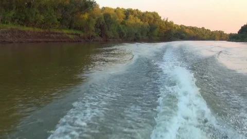 Wake from the propeller of a boat moving on a dull desert the river along steep Stock Footage 79358491