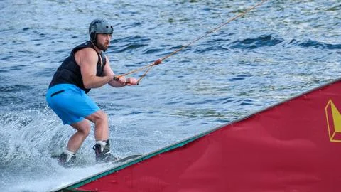 Wakeboarder approaching kicker obstacle at cable wake park Stock Photos