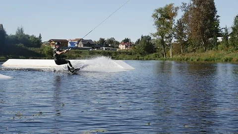Wakeboarder guy riding on string jumping on ramp on lake Stock Footage 85999455