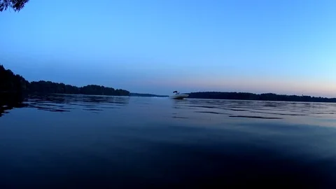 A wakeboarder jumps the wake behind a speed boat, summer dusk sky, long shot Stock Footage 74950609