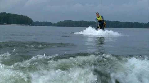 Wakeboarder man in diving suit jumps the wake behind a motor boat Stock Footage 67007342