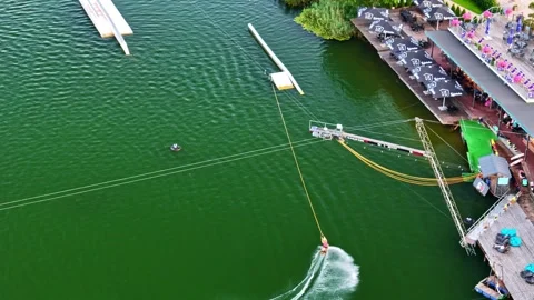 Wakeboarder rides cable park over green water near shoreline bar in Ozolnieki Stock Footage 317092029