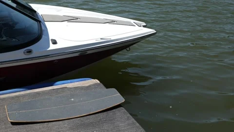 Wakeskate board lying next to a wakeboard boat which is docked at the pier. Video stock 201365963