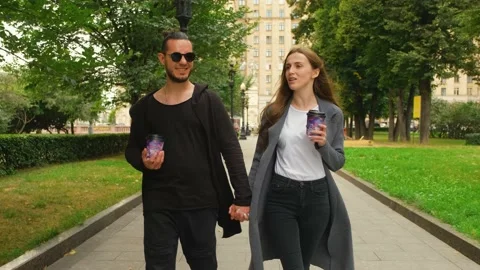 A walk in the park of a nice guy and a girl with coffee in their hands. Video stock 139883942