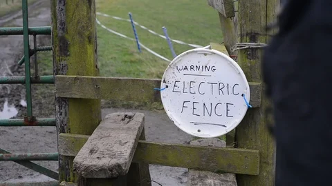 Walker climbing over style by warning sign of electric fence uk Stock Footage 86233347