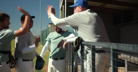 Walking African American player tossing baseball by dugout, starting coach Stock Footage 336658064