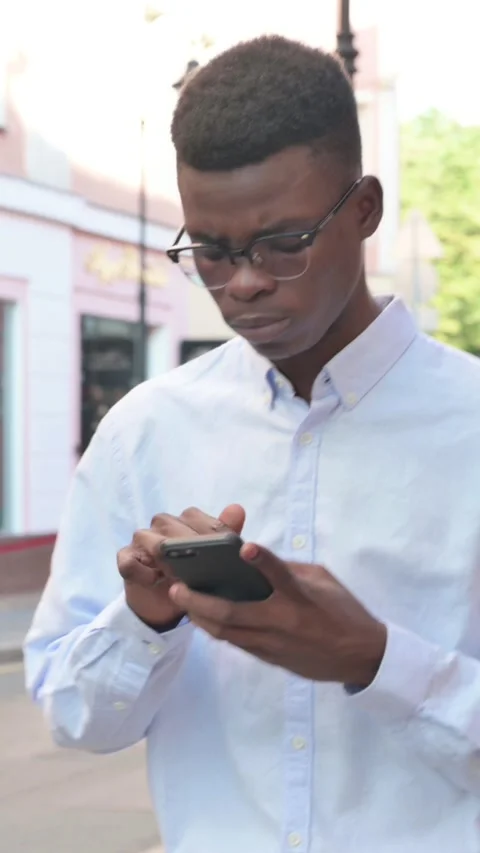 Walking African Man Browsing Internet on Smartphone, Vertical Video Stock Footage 340022458