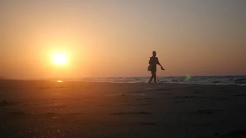 Walking alone on a sandy beach by the sea on a beautiful sunset in the golden Stock Footage 80231563
